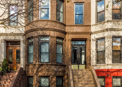 Classic brownstone building with ornate detailing, bay windows, and a stoop with wrought iron railings