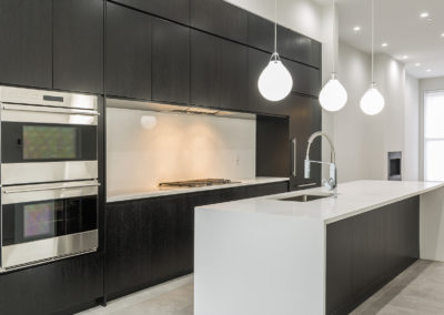 Sleek minimalist kitchen with black cabinets, white countertops, pendant lights, and built-in stainless steel appliances.