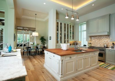 Modern kitchen designed with green cabinets, hardwood floors, butcher block island, marble countertops, and pendant lighting.