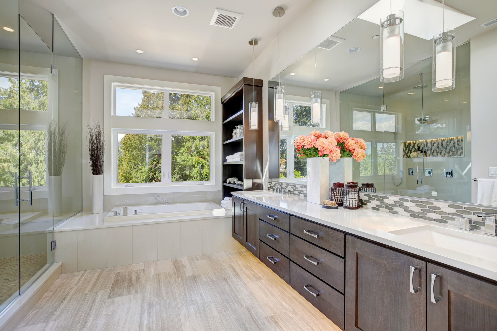 Modern bathroom with dual vanity, glass shower, and a view of greenery outside.