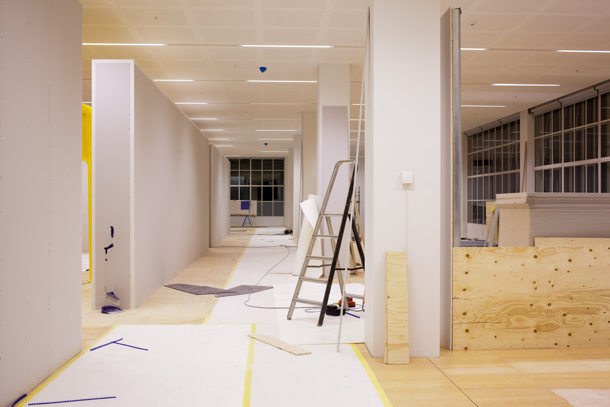 Interior construction site with drywall partitions, a ladder, and materials on the floor.