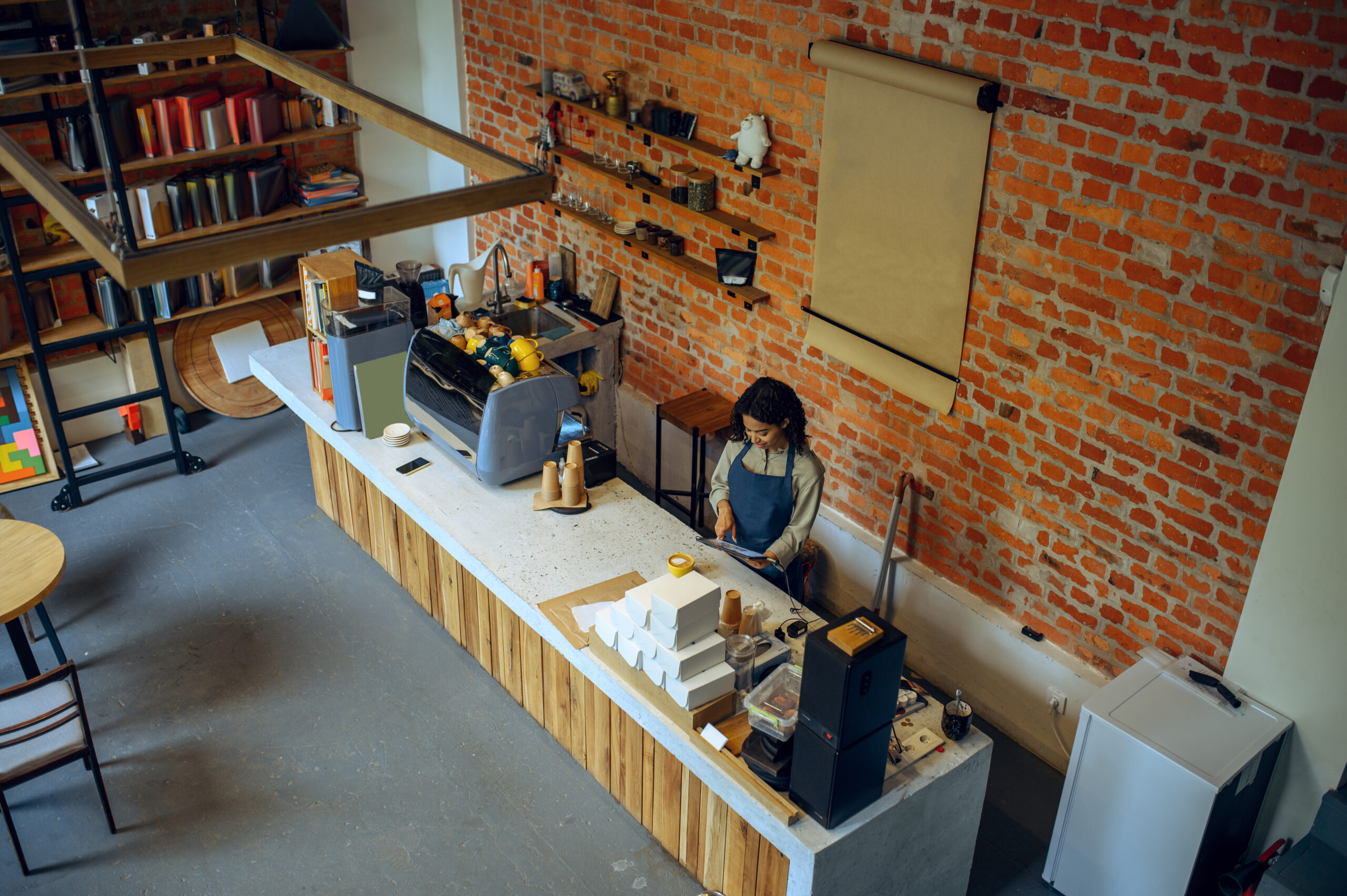 A focused female barista prepares orders in a charming café with exposed brick and a cozy loft vibe.