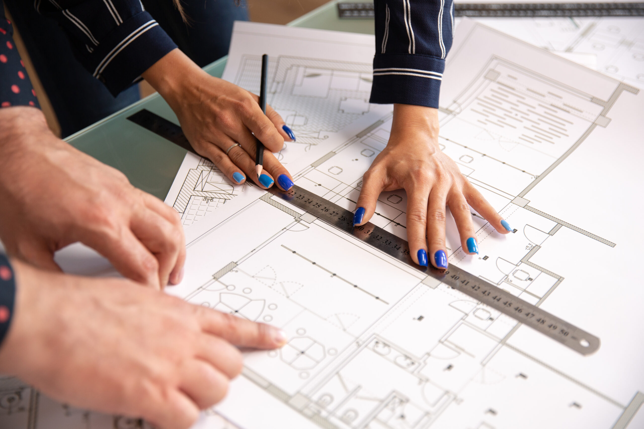 Two architects working on a blueprint with a ruler and pencil.