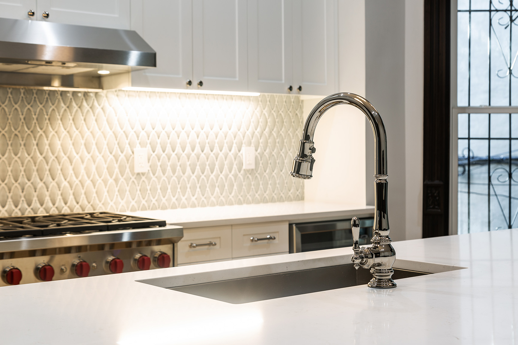 Close-up of kitchen sink with stylish faucet, tiled backsplash, and a view to stained glass windows.