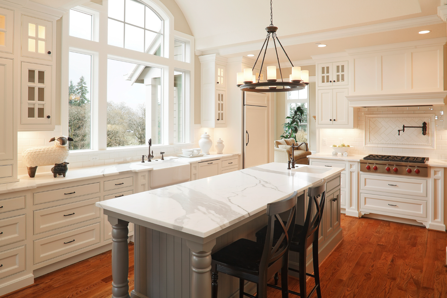 Spacious, well-lit kitchen with white cabinetry, marble countertops, and large windows.