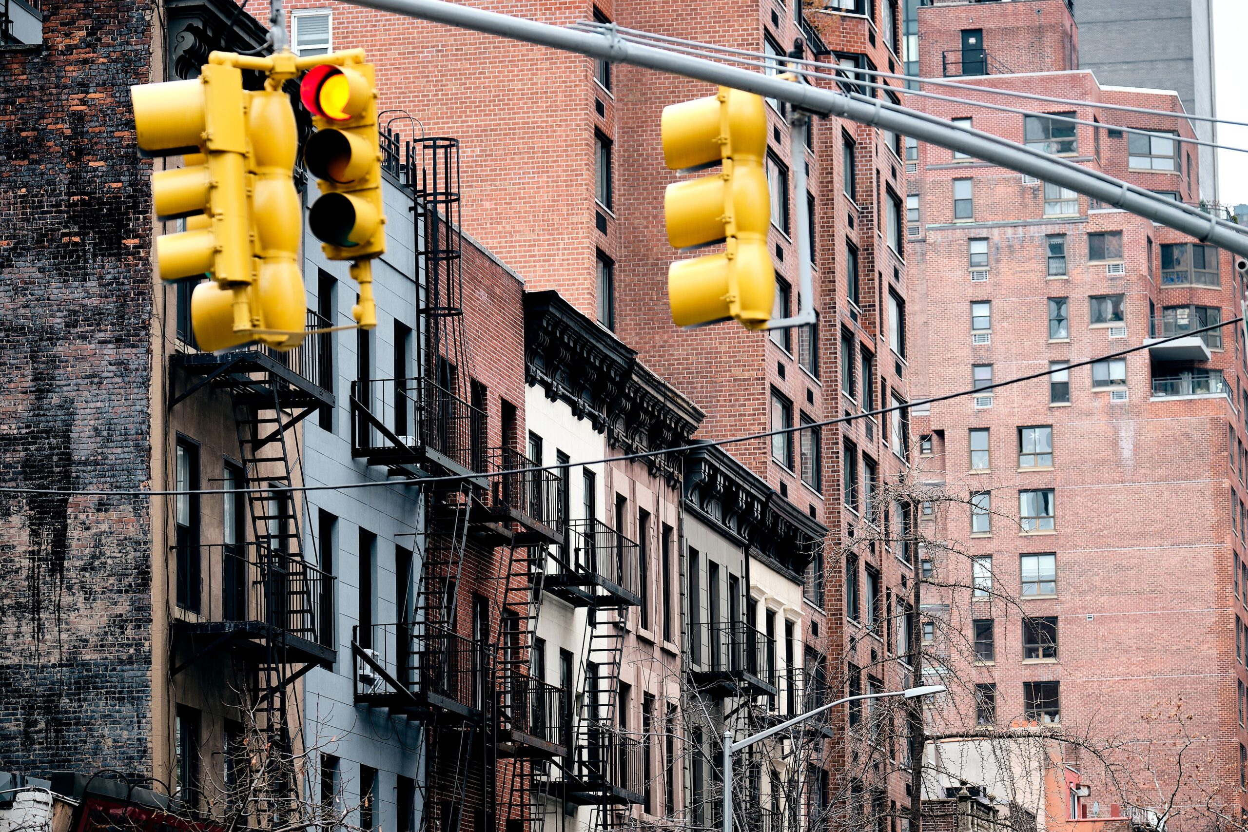 Traffic lights against a backdrop of contrasting brick buildings and fire escapes.