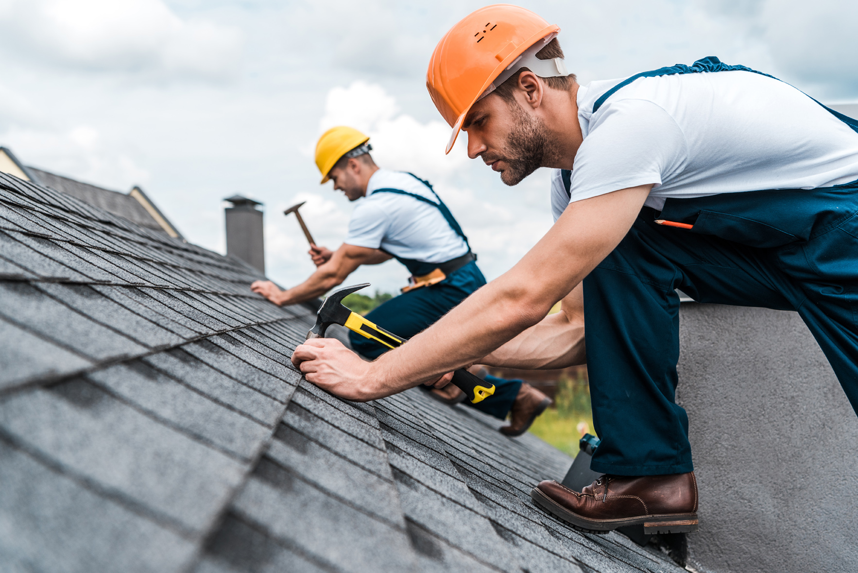 Workers in hard hats installing shingles on a steep roof.