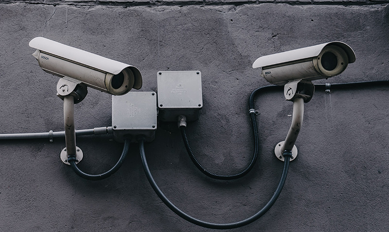 Two security cameras mounted on a dark textured wall, cables neatly arranged.