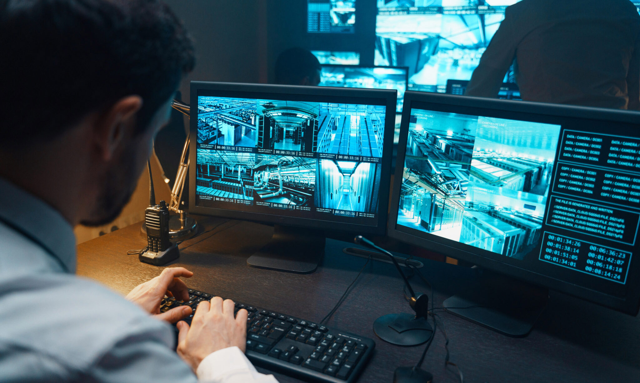 A focused individual at a surveillance workstation, monitoring a multi-screen setup with various camera feeds, indicative of a comprehensive security system